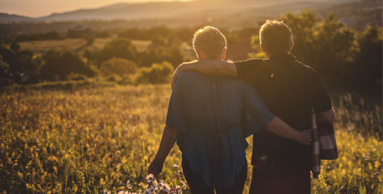Couple with arms around each other walking toward sunset